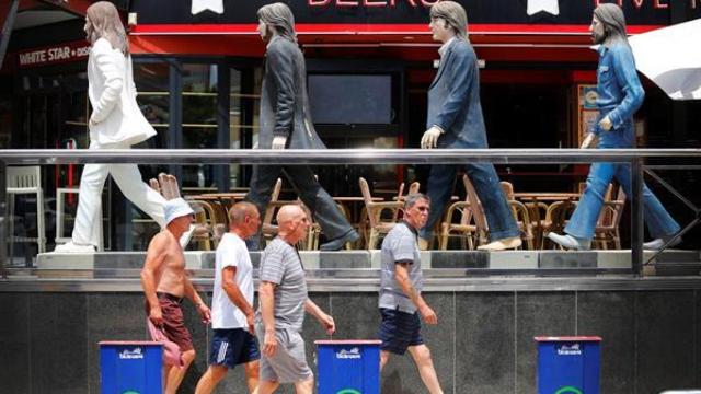 Cuatro personas pasan ante una cervecería de Benidorm que usa como reclamo las figuras de The Beatles.